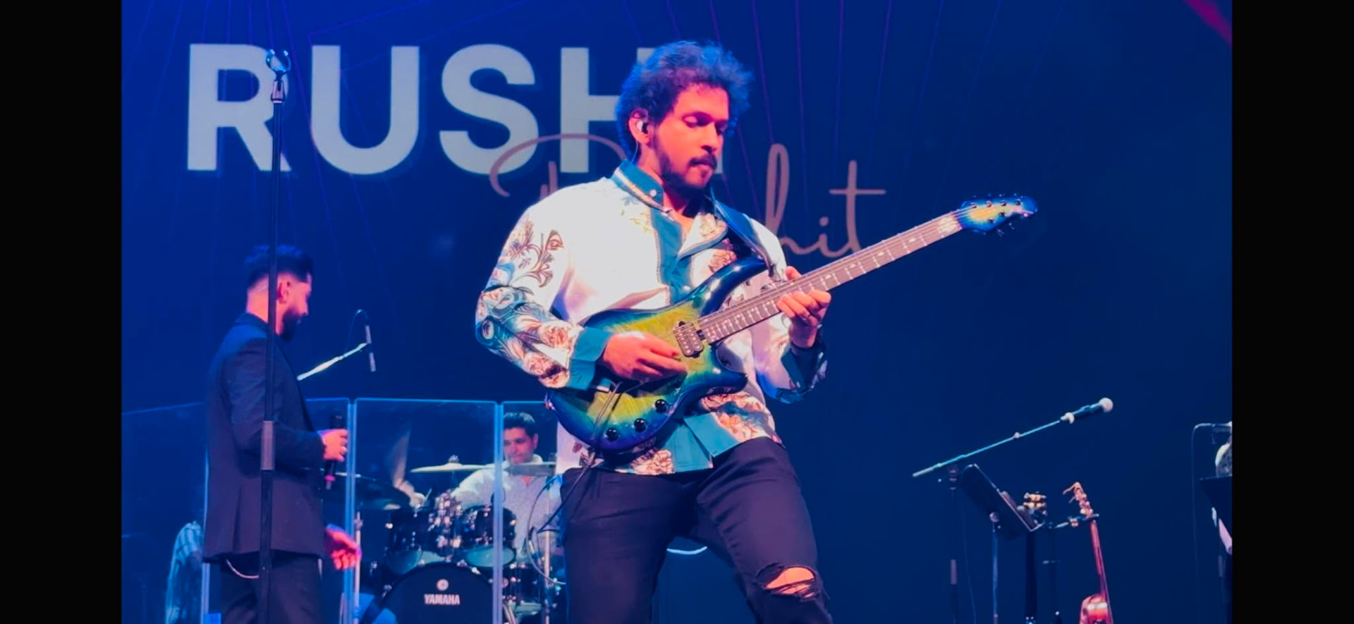 Glen Fernandez playing electric guitar under amber stage lights