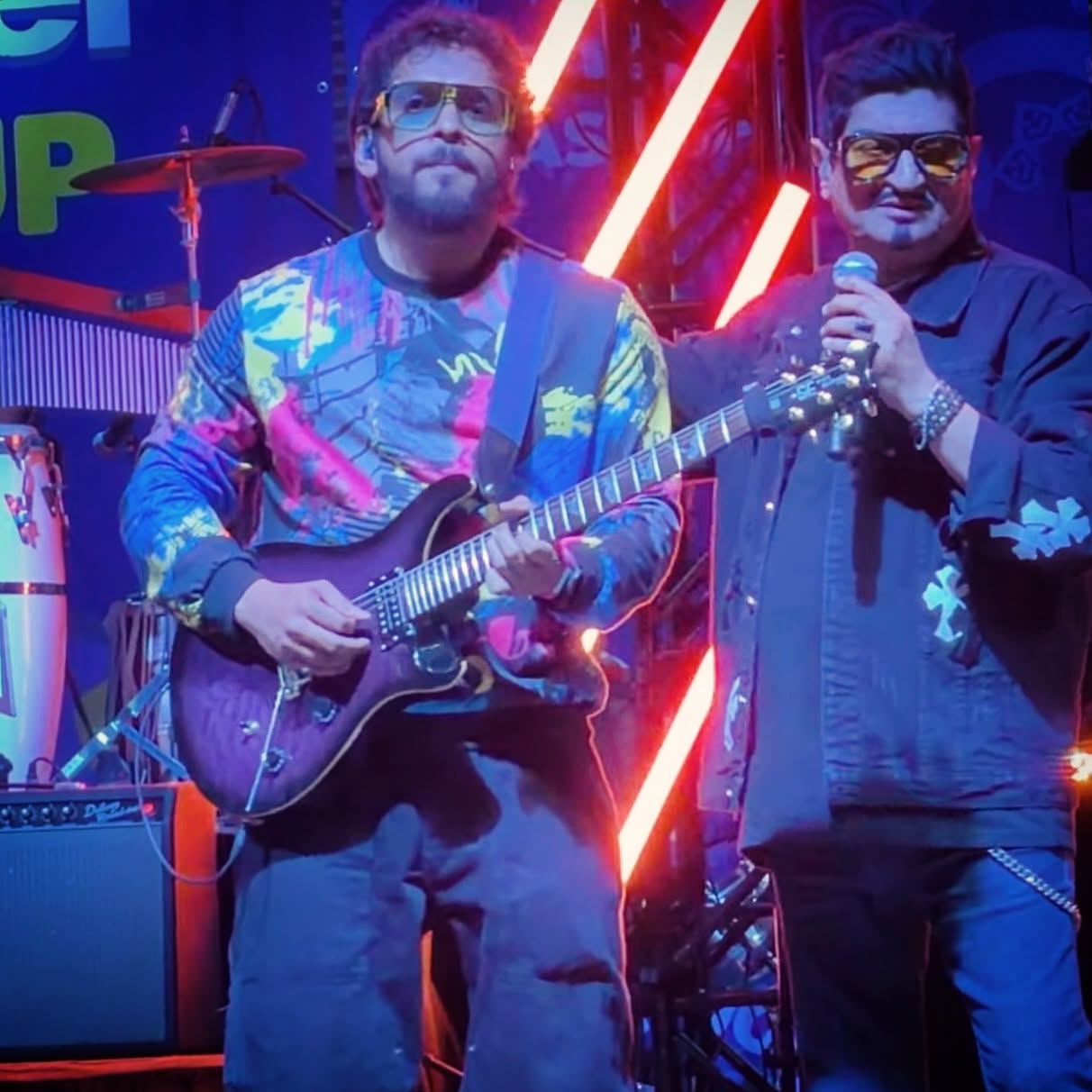 Glen Fernandez performing beside a vocalist under neon lights